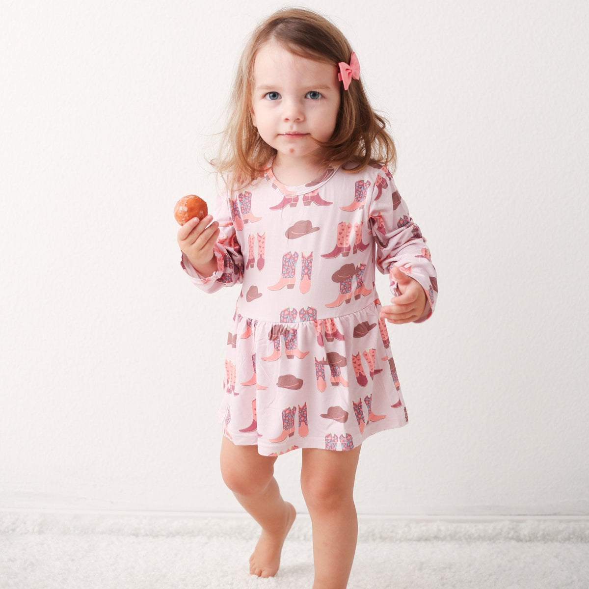 Bodysuit dress with long sleeves in pink, printed with cowboy boots and hats, worn by a toddler