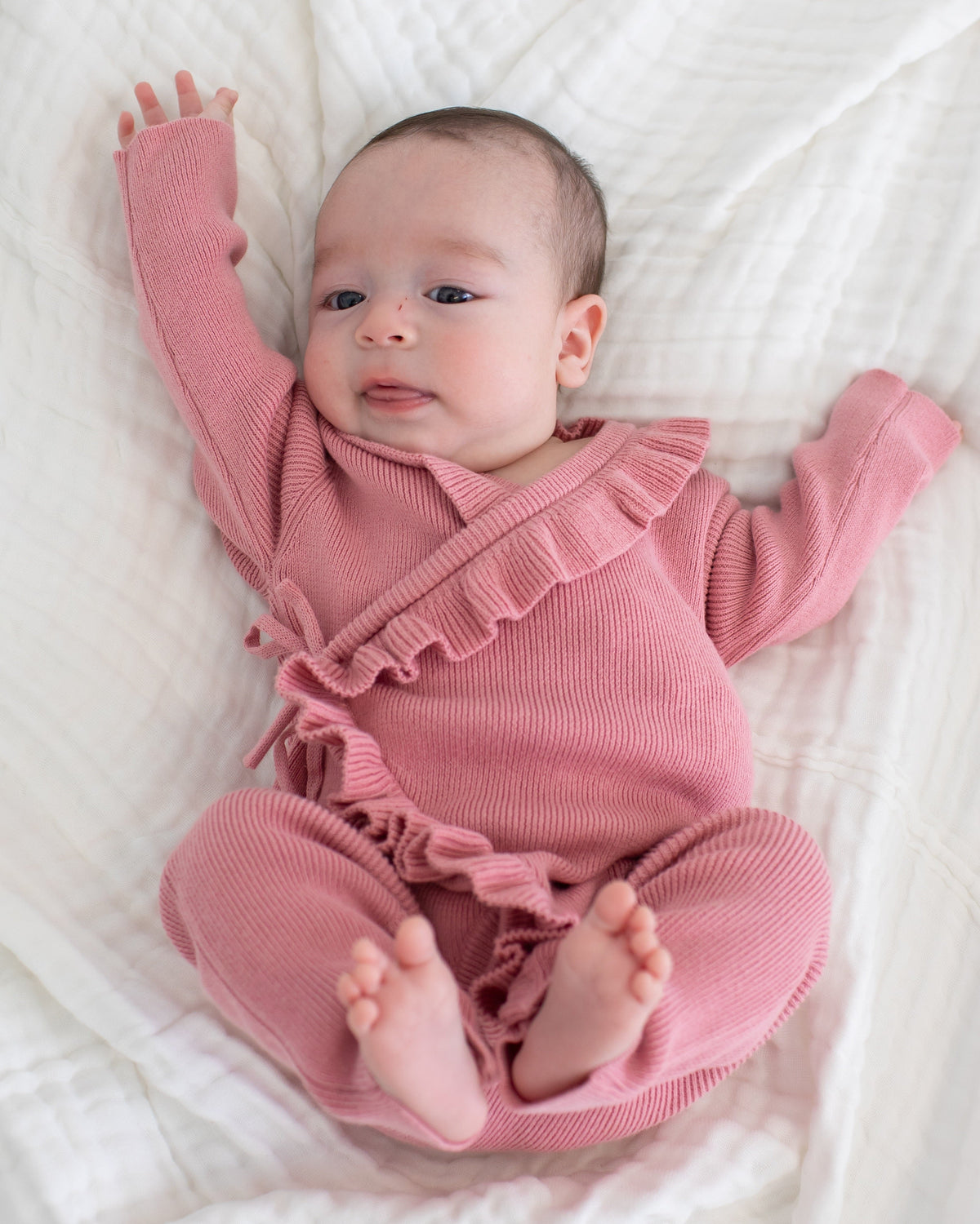 Baby wrap romper in dusty rose with ruffle trim along the neckline and wrap front, tied at the side