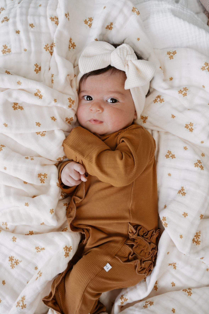 Baby wearing a caramel ribbed ruffle zipper one-piece on a floral blanket.