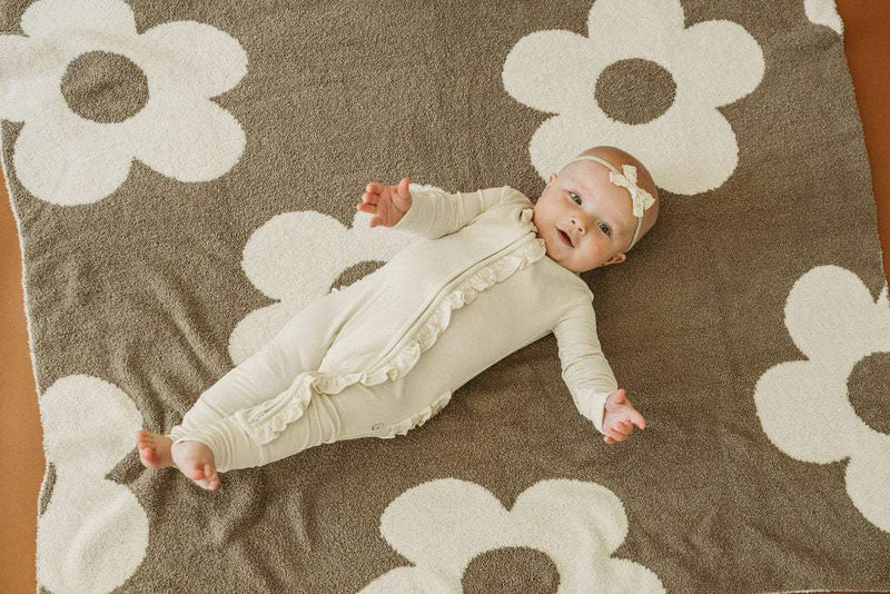 Cream bamboo ruffle zipper one piece outfit for baby with fold-over cuffs, lying on patterned blanket.