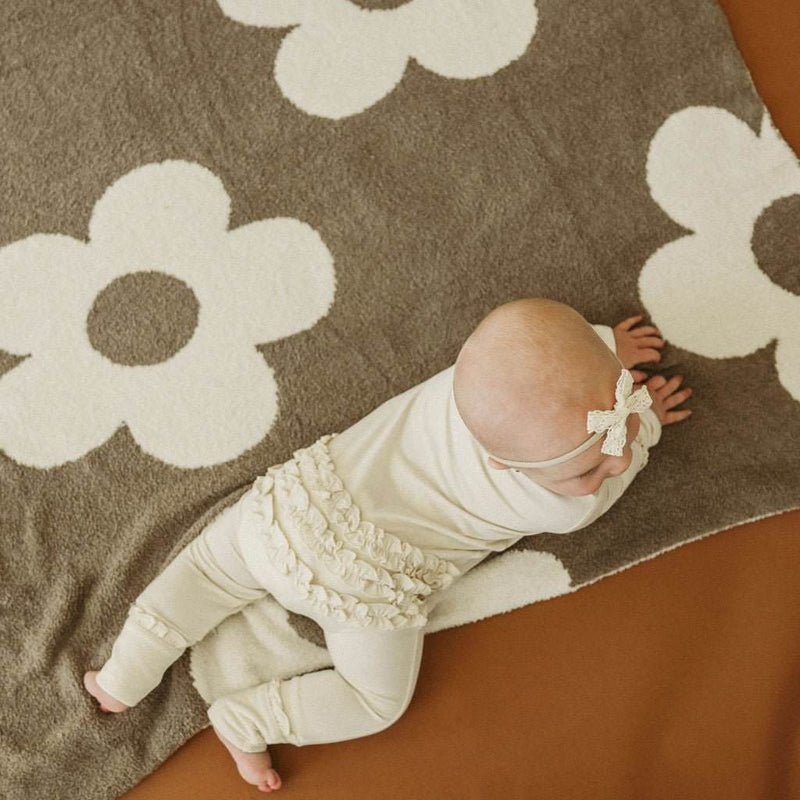 Cream ruffle zipper one piece outfit for babies on floral blanket.
