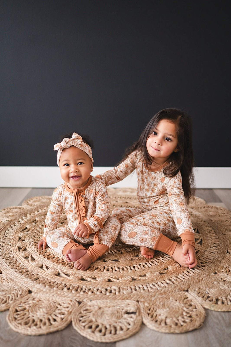 Baby wearing Ruffle Zipper One Piece Flower Garden outfit with bamboo fabric and ruffle details, seated on a decorative rug.
