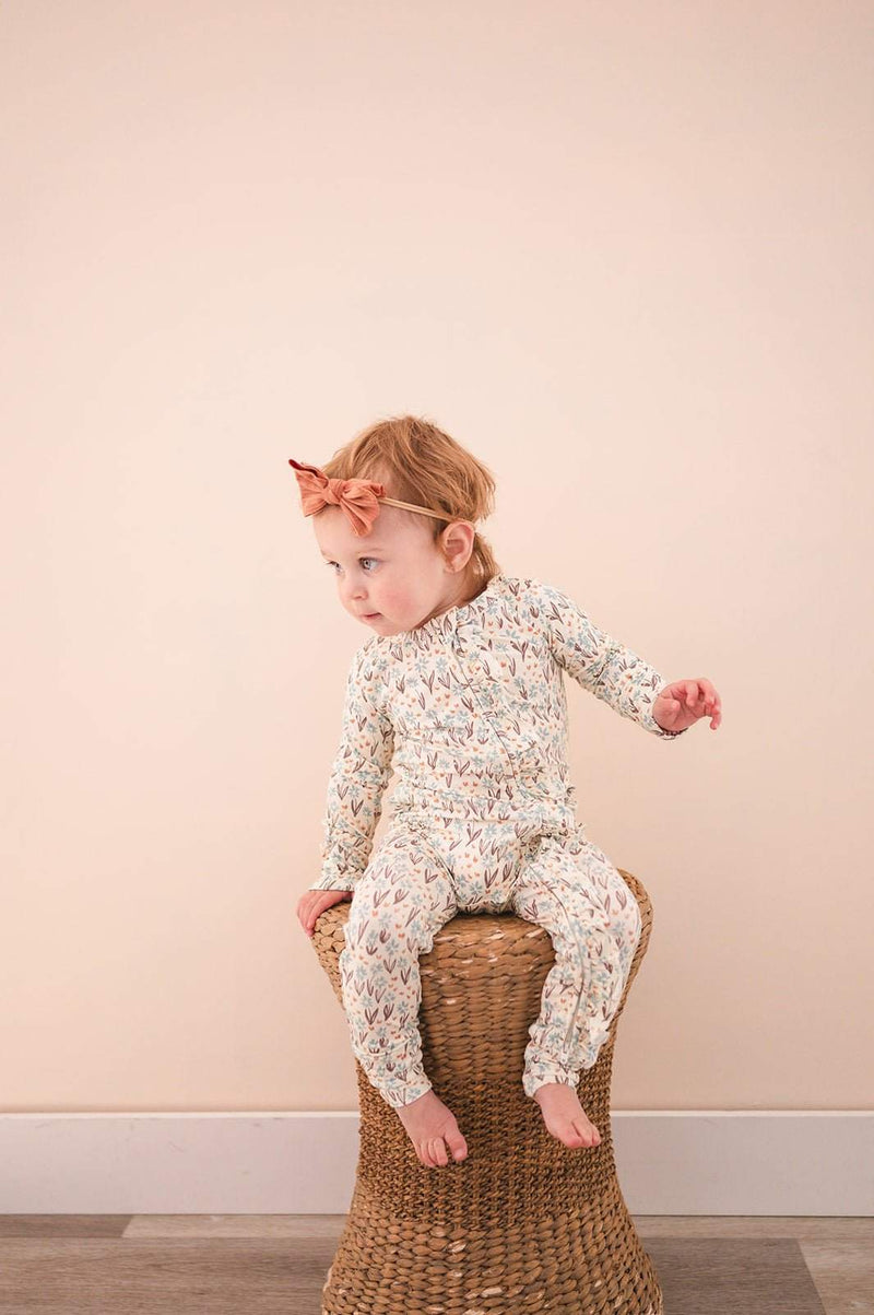 Ruffle Zipper One Piece in La La Floral design with ruffle details and 2-way zipper, worn by a baby on a wicker stool.