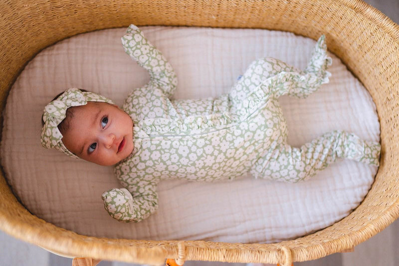 Baby wearing Ruffle Zipper One Piece in sage ditsy floral design laying in a wicker basket.