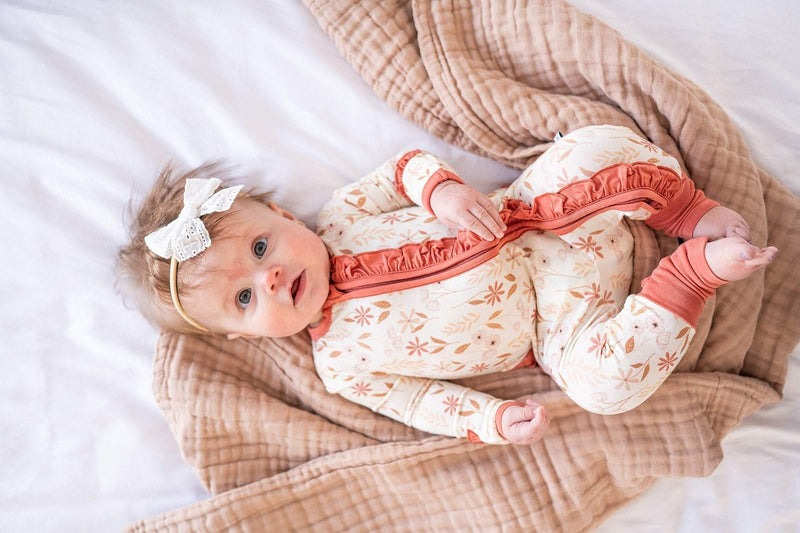 Baby wearing Ruffle Zipper One Piece in Wildflower print, lying on a plush blanket.