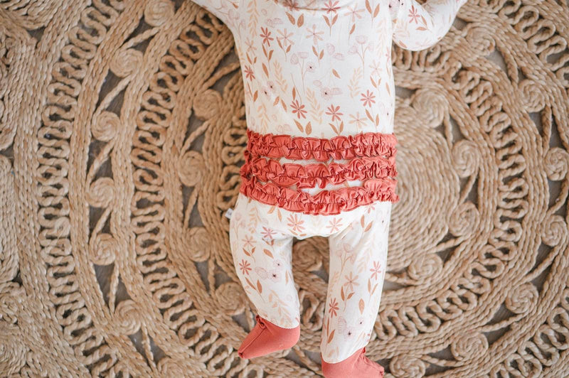 Wildflower bamboo baby one piece with ruffle details and zipper on woven mat.
