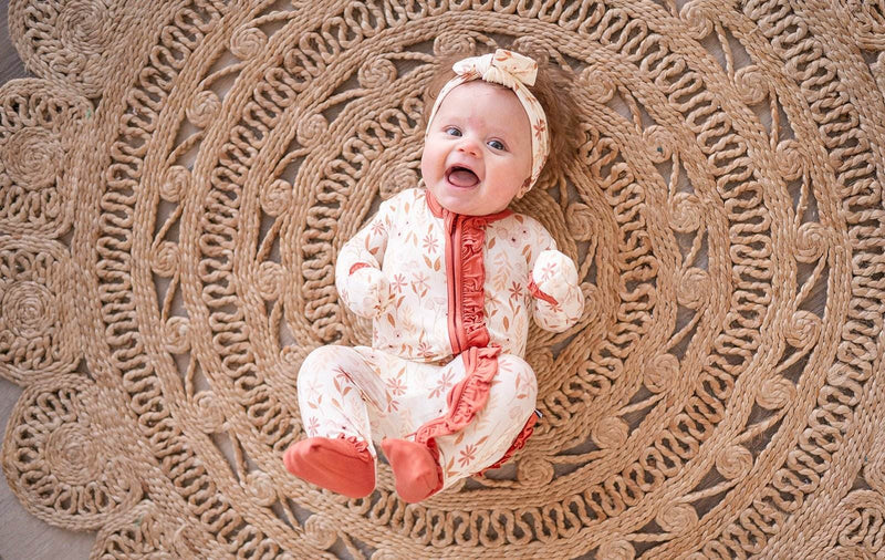 Baby wearing Wildflower Bamboo Ruffle Zipper One Piece romper on a woven mat.