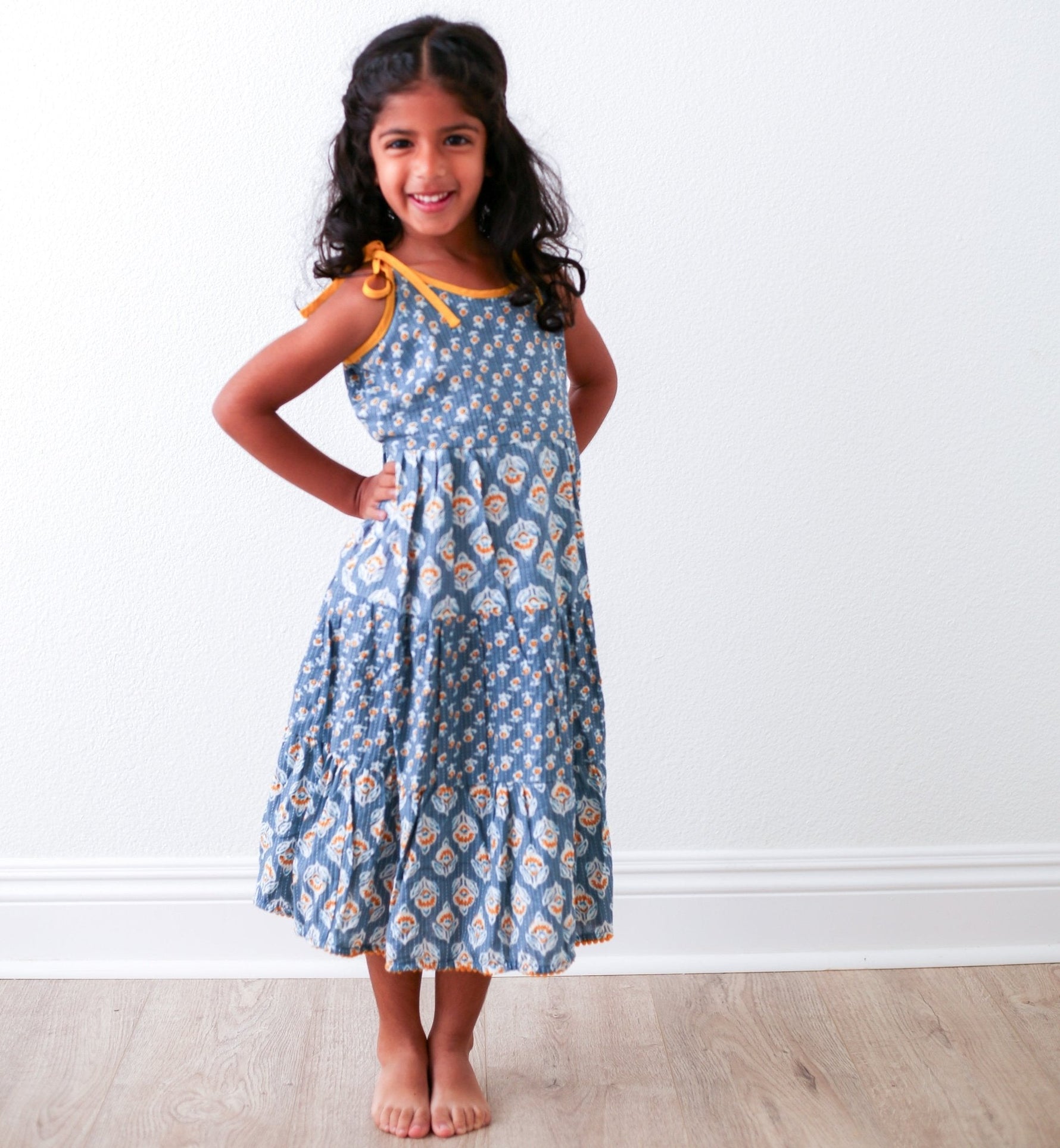 Blue maxi dress with a Bohemian block print pattern and adjustable tie straps, worn by a smiling child.