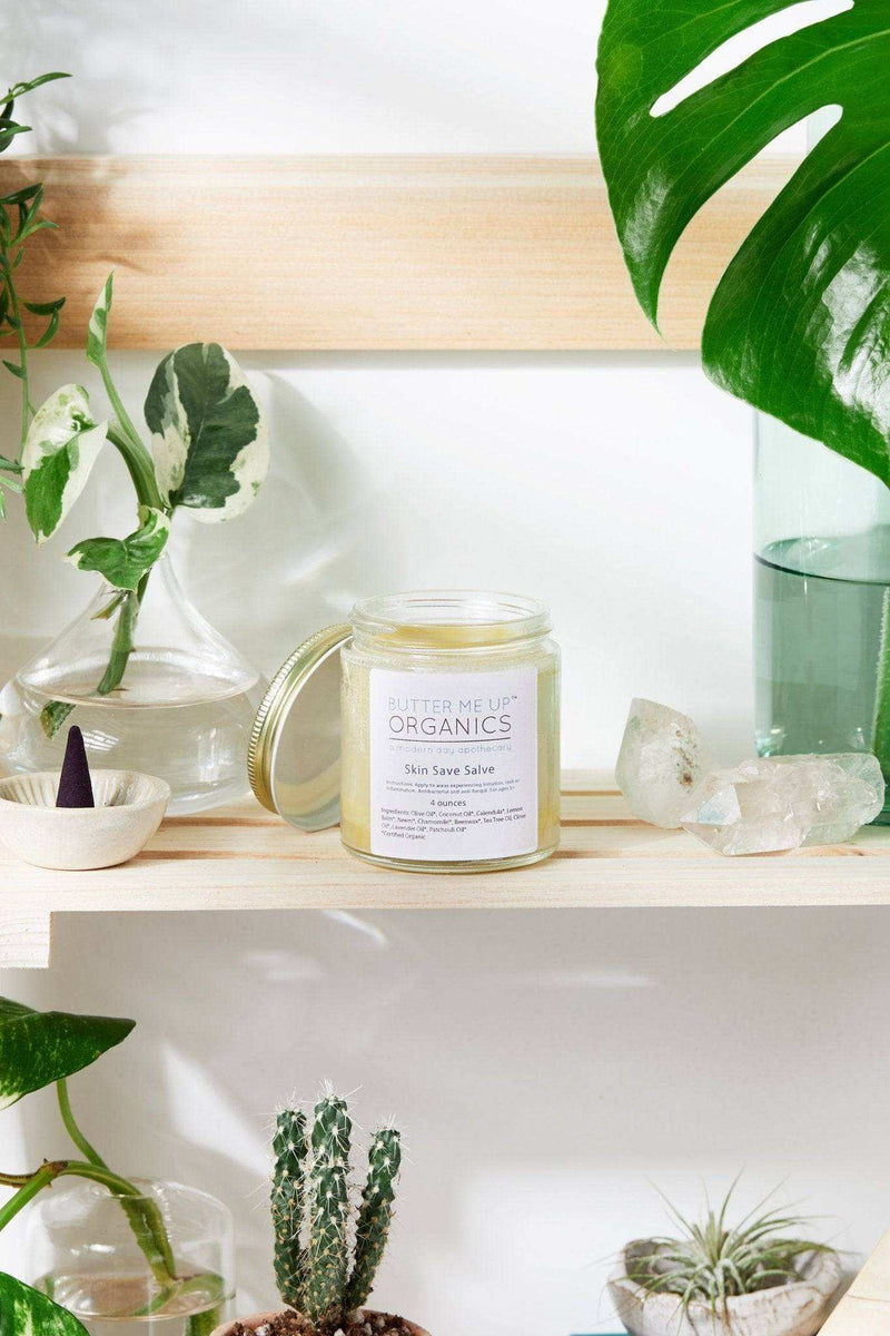 Organic Skin Save Salve jar on a wooden shelf surrounded by plants and crystals.