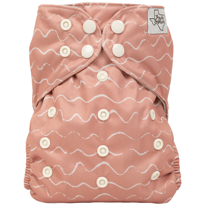 Slim fit AIO cloth diaper in pink with snap closures and wave pattern.