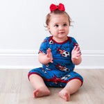 Baby shortall romper with soccer ball print, lap shoulder neckline, and snaps along the legs.