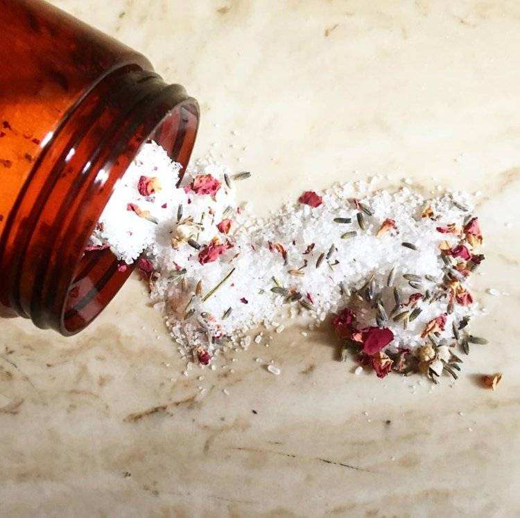 Soothe + Relax Bath Soak with rose petals and lavender on a marble surface.