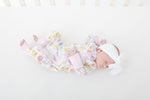 Baby zip-up pajamas in an Italian-inspired print with pink scooters, citrus, palm trees, seashells, and postcards.
