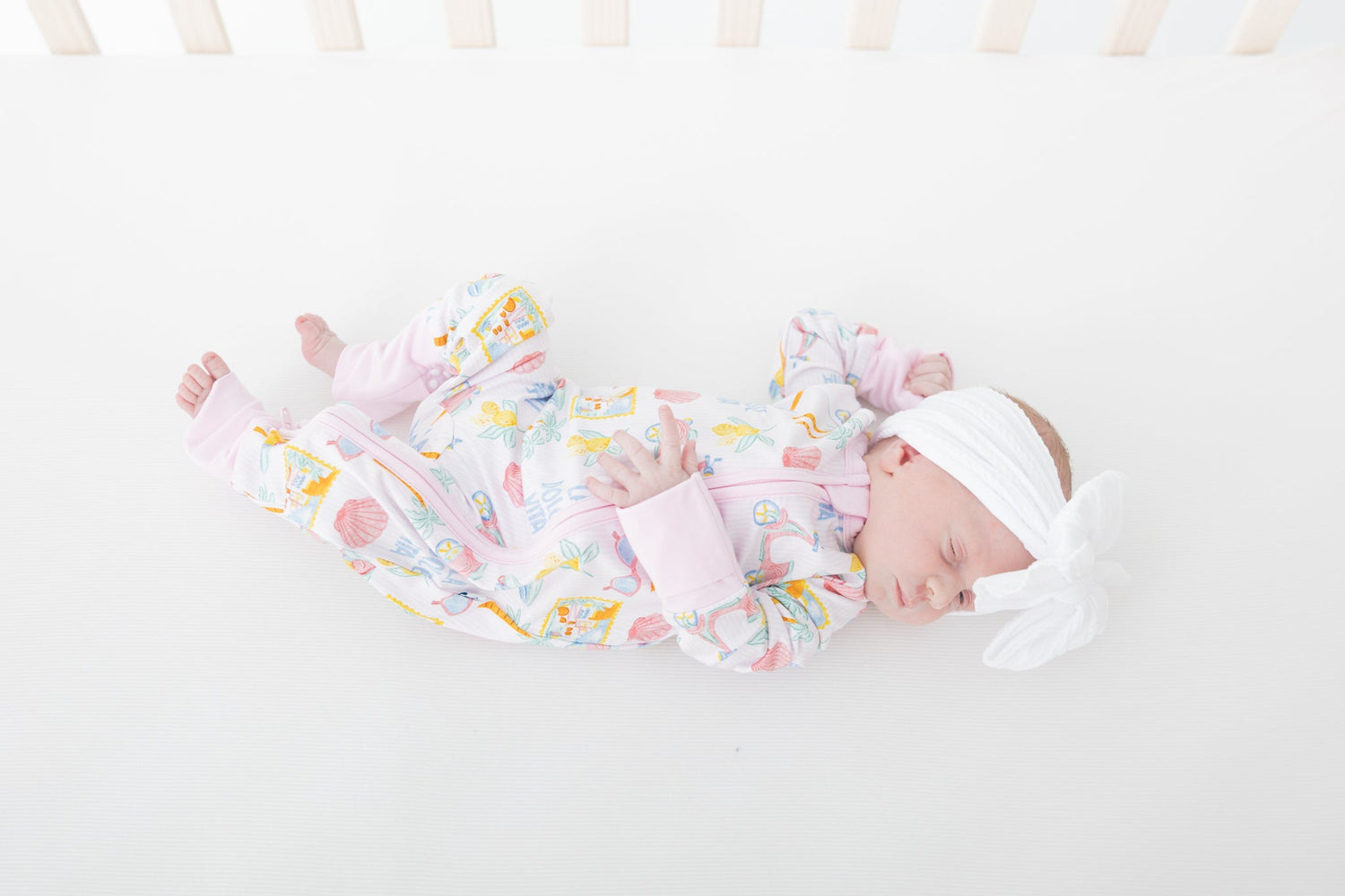 Baby zip-up pajamas in an Italian-inspired print with pink scooters, citrus, palm trees, seashells, and postcards.