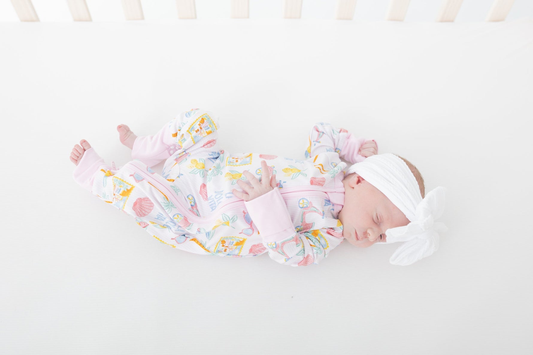 Baby zip-up pajamas in an Italian-inspired print with pink scooters, citrus, palm trees, seashells, and postcards.