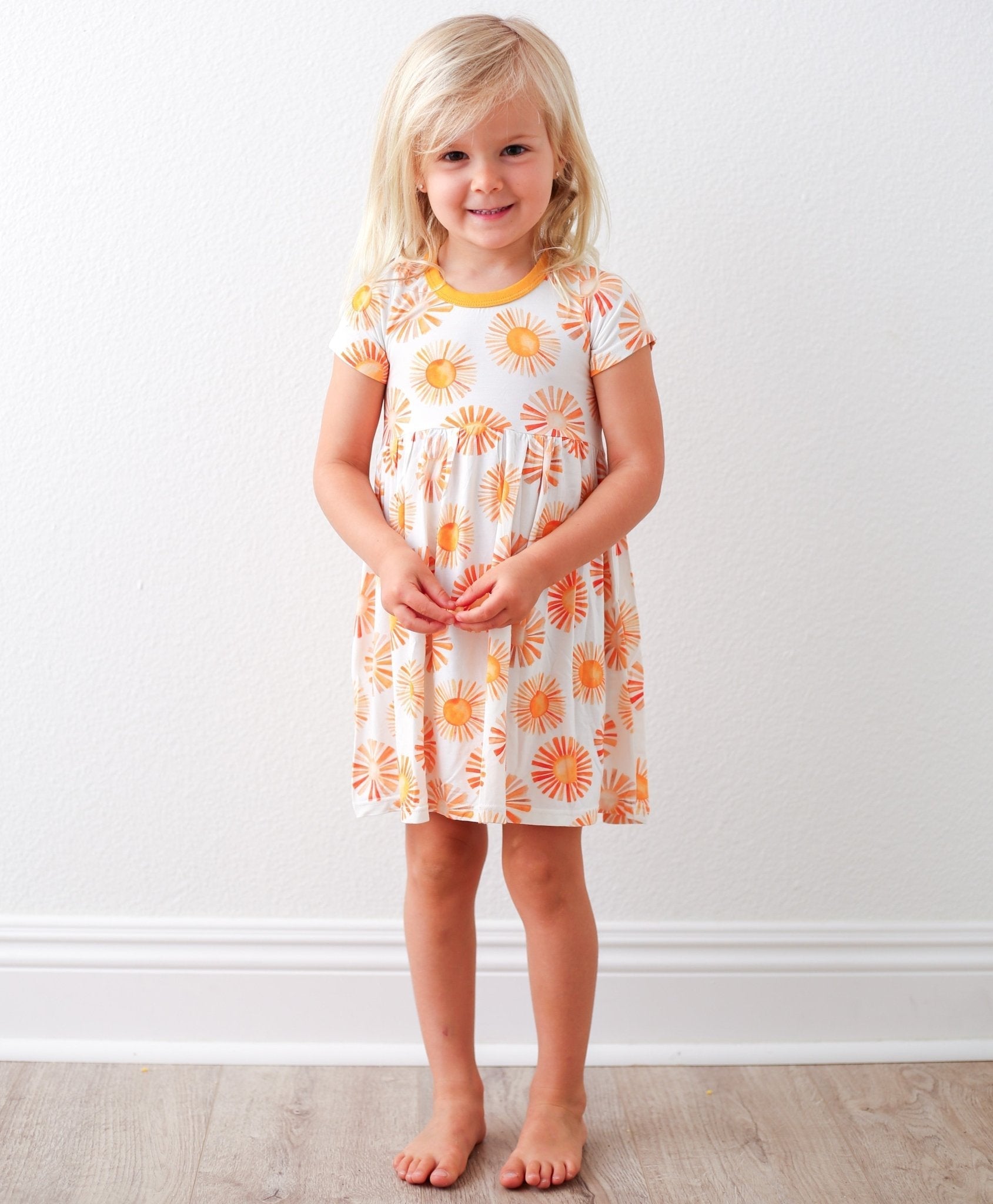 Short sleeve toddler dress with a bright pink and yellow sunshine print, worn by a young child.