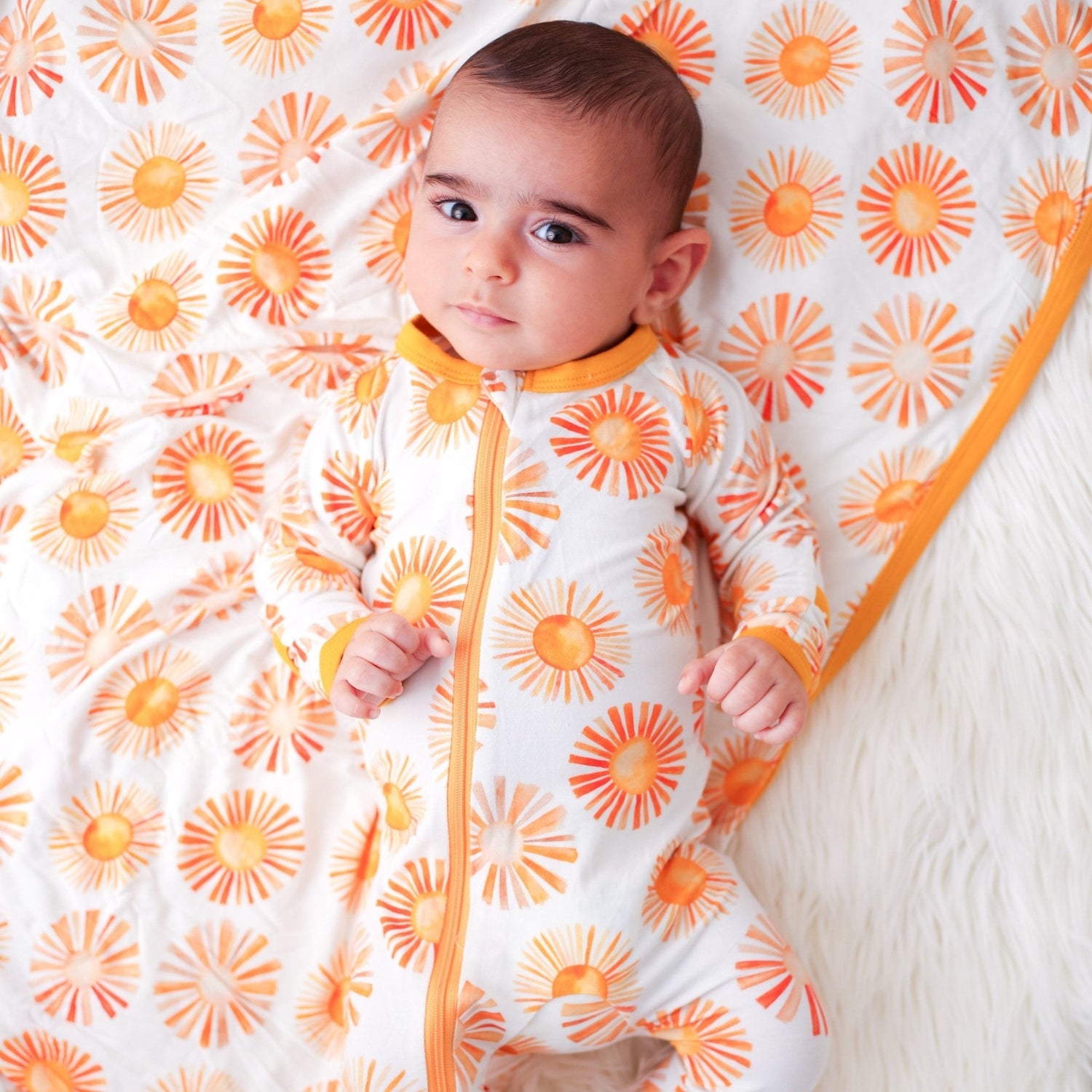 Baby footie pajamas with full-length zipper and covered feet in a soft light color.
