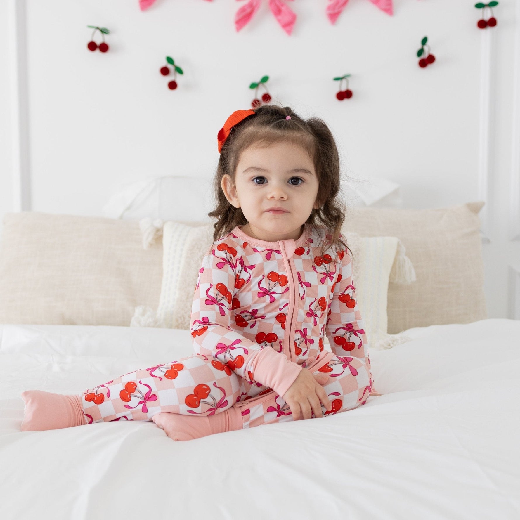 Baby romper in pink checker bamboo fabric with cherries and bows, featuring a two-way zipper and fold-over feet.