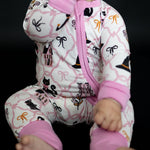 Baby romper in soft pink with black cats, witch hats, and pastel bows, fold-over cuffs and a front zipper.