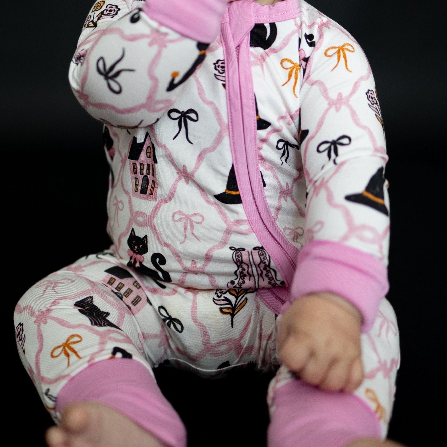 Baby romper in soft pink with black cats, witch hats, and pastel bows, fold-over cuffs and a front zipper.