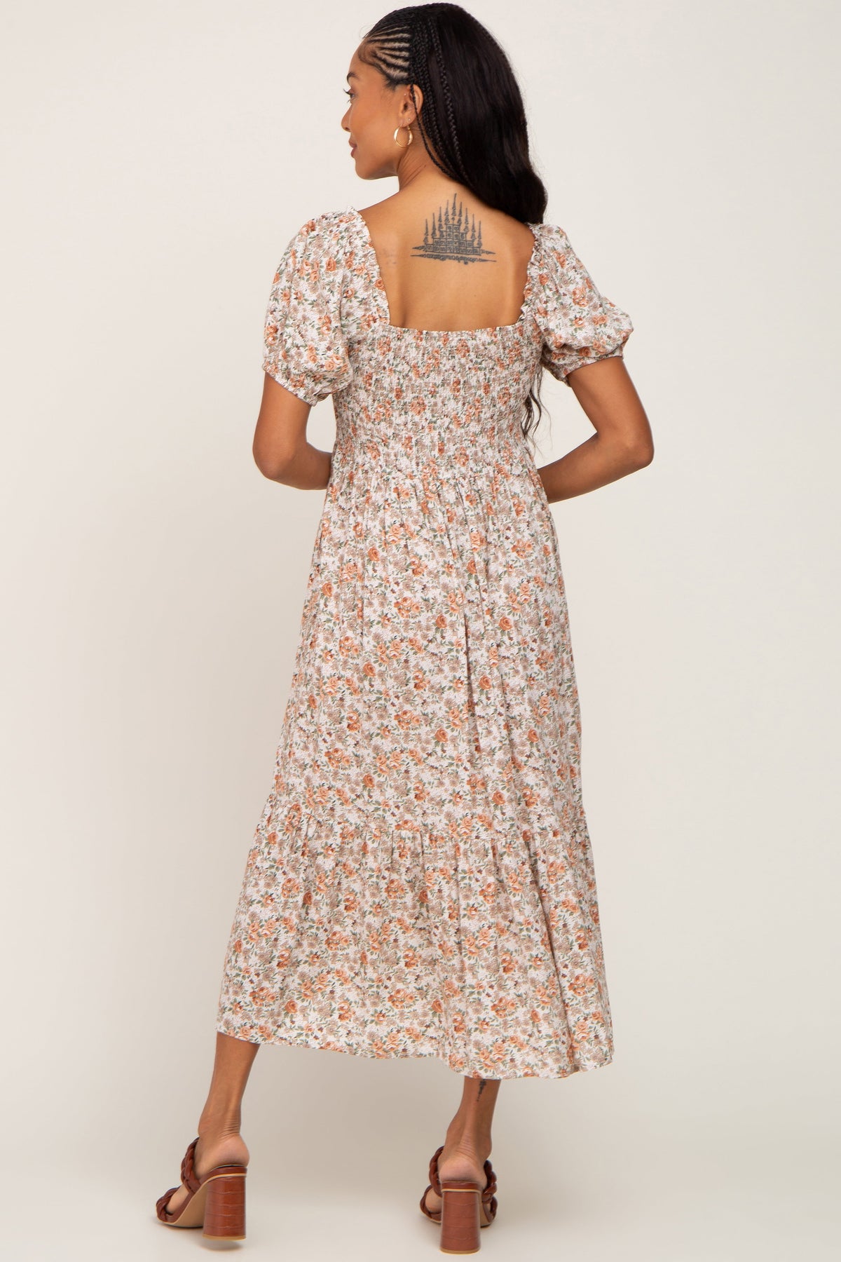 Model wearing a taupe floral smocked puff sleeve midi dress, standing in a natural setting.