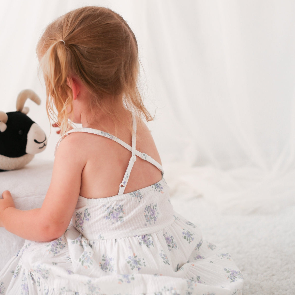 White floral print baby dress with racer back, shown on a child model holding a stuffed toy