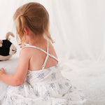 White floral print baby dress with racer back, shown on a child model holding a stuffed toy