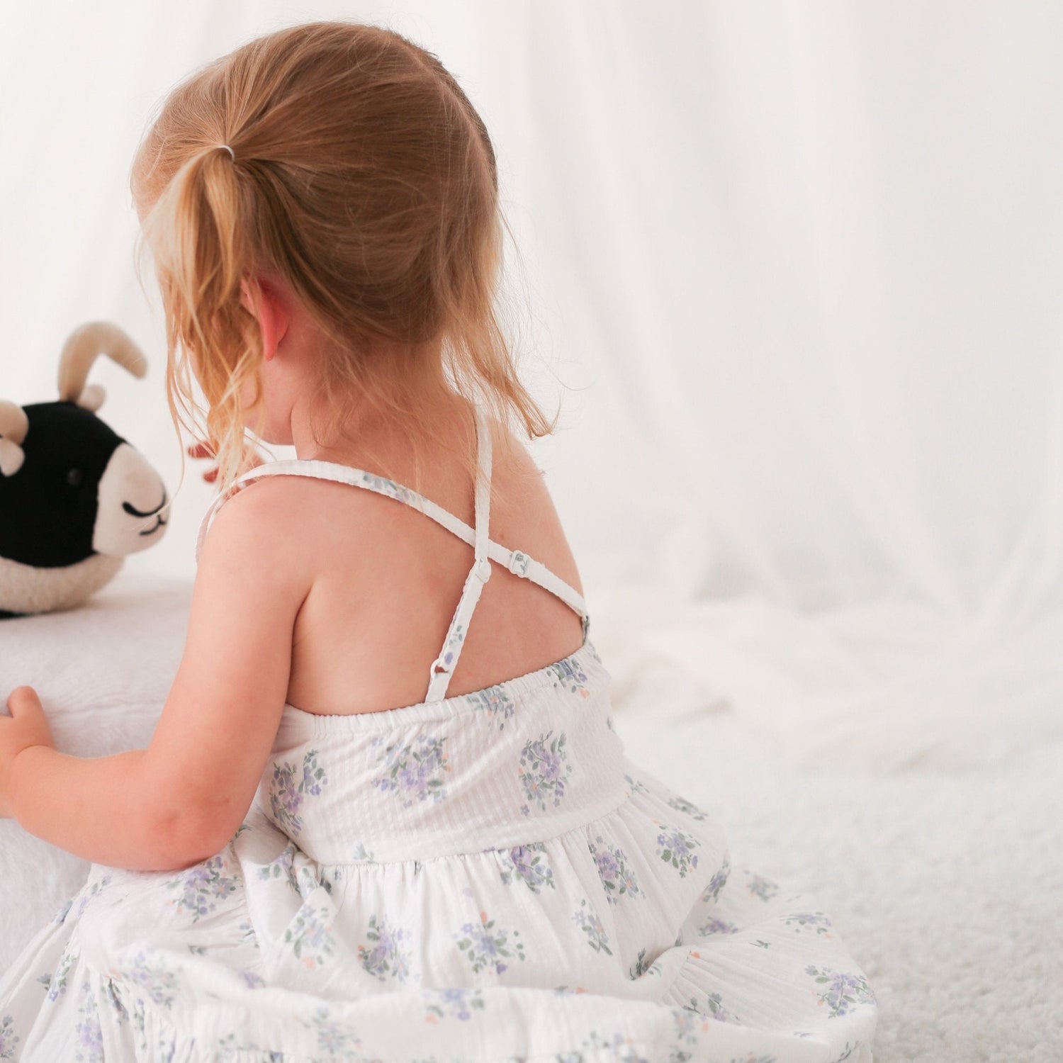 White floral print baby dress with racer back, shown on a child model holding a stuffed toy
