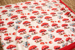 Baby swaddle blanket with red and cream toadstool mushroom print, spread flat to show the pattern.