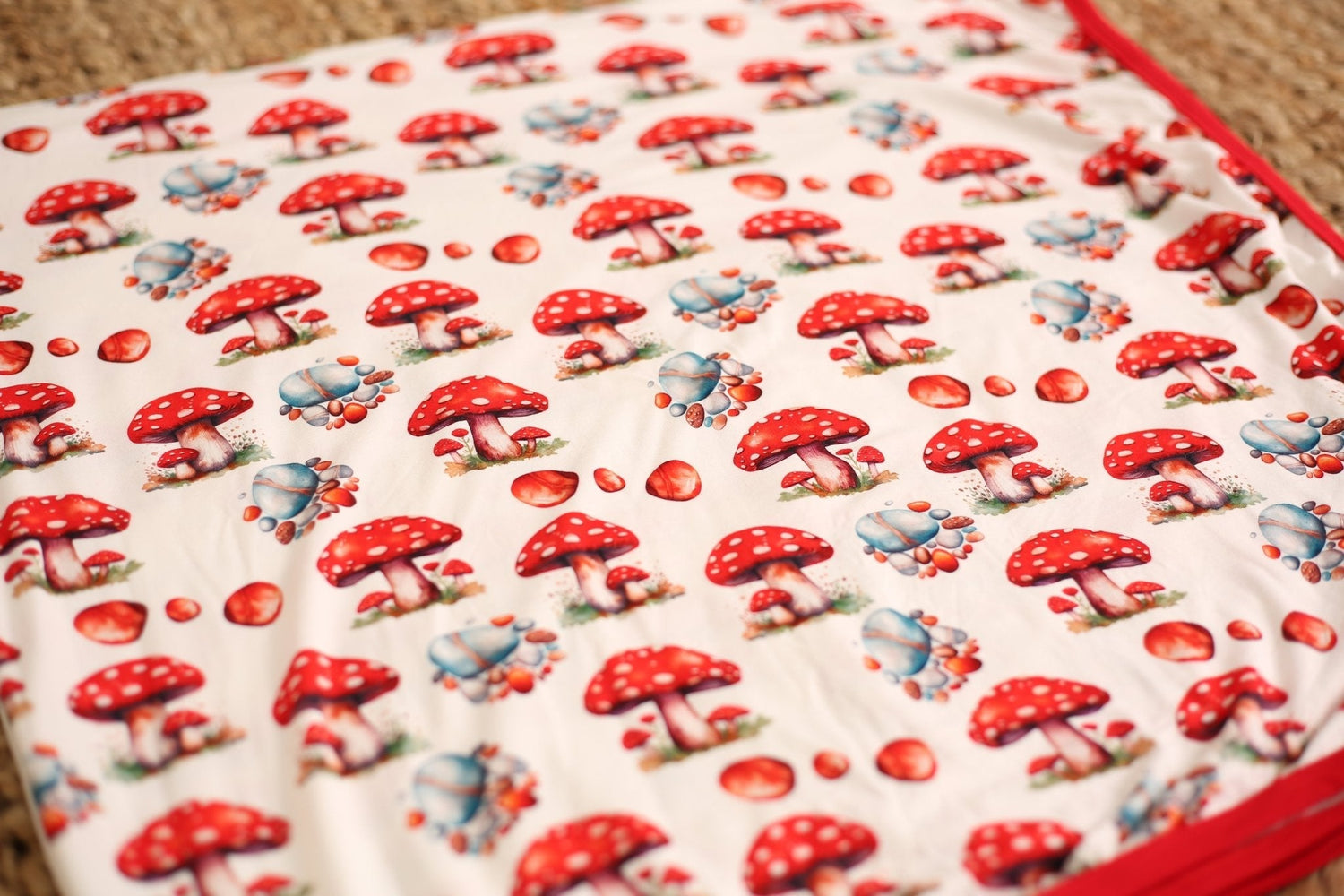 Baby swaddle blanket with red and cream toadstool mushroom print, spread flat to show the pattern.