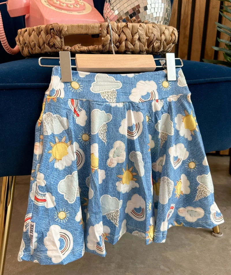 Twirl Skorts with blue sky and cloud pattern hanging on display.