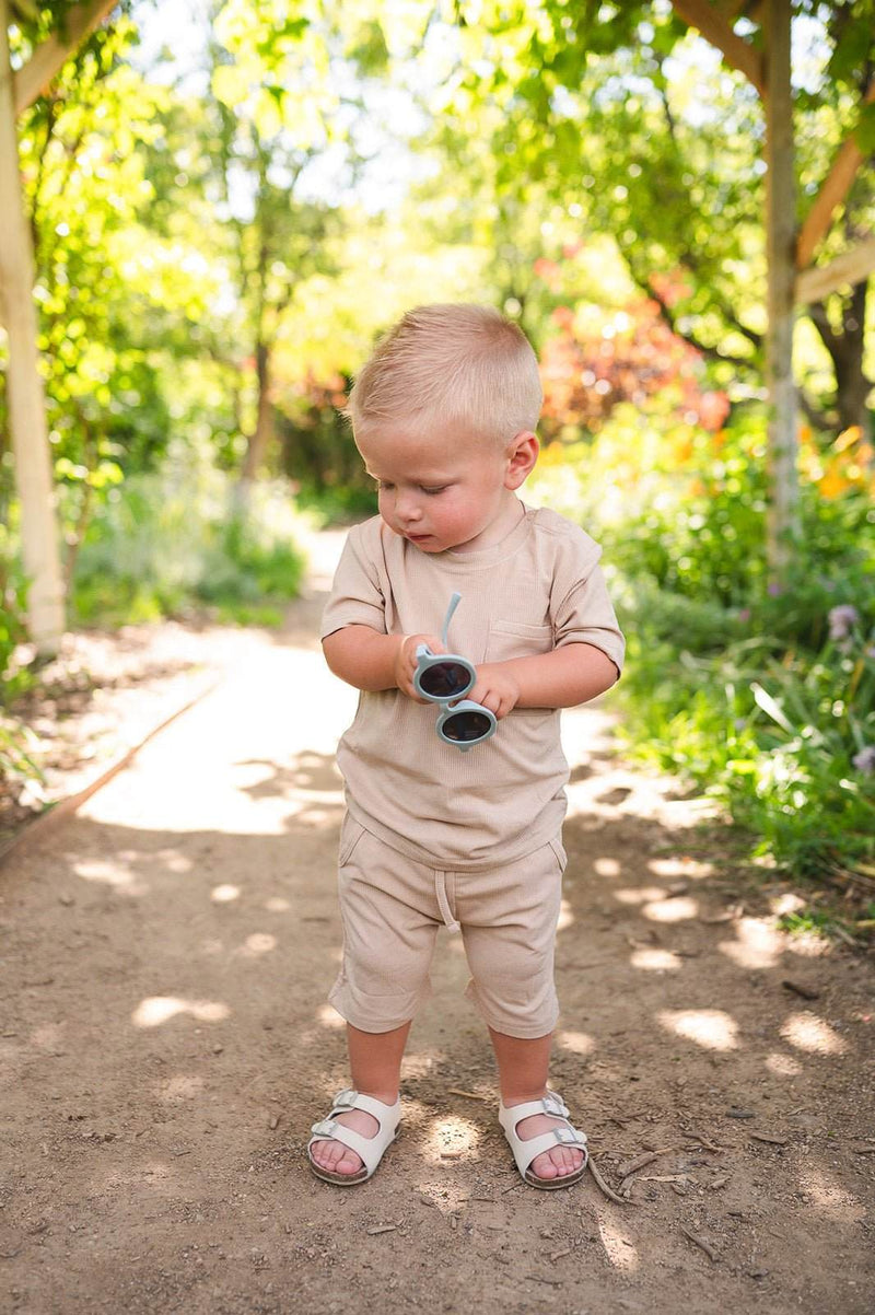 Tan two-piece ribbed short set for toddlers with pocket shirt and shorts, made of bamboo and spandex, shown outdoors.