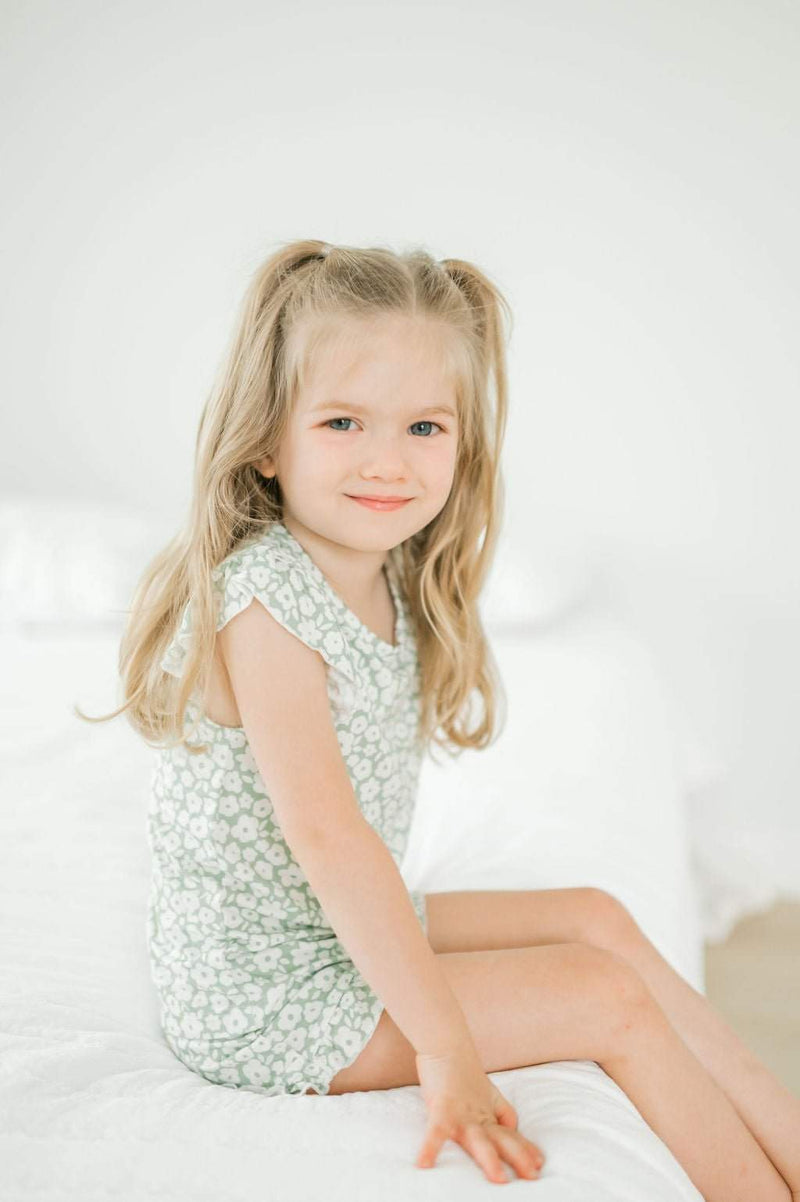 Two-piece short set in sage ditsy floral on a child sitting on bed.