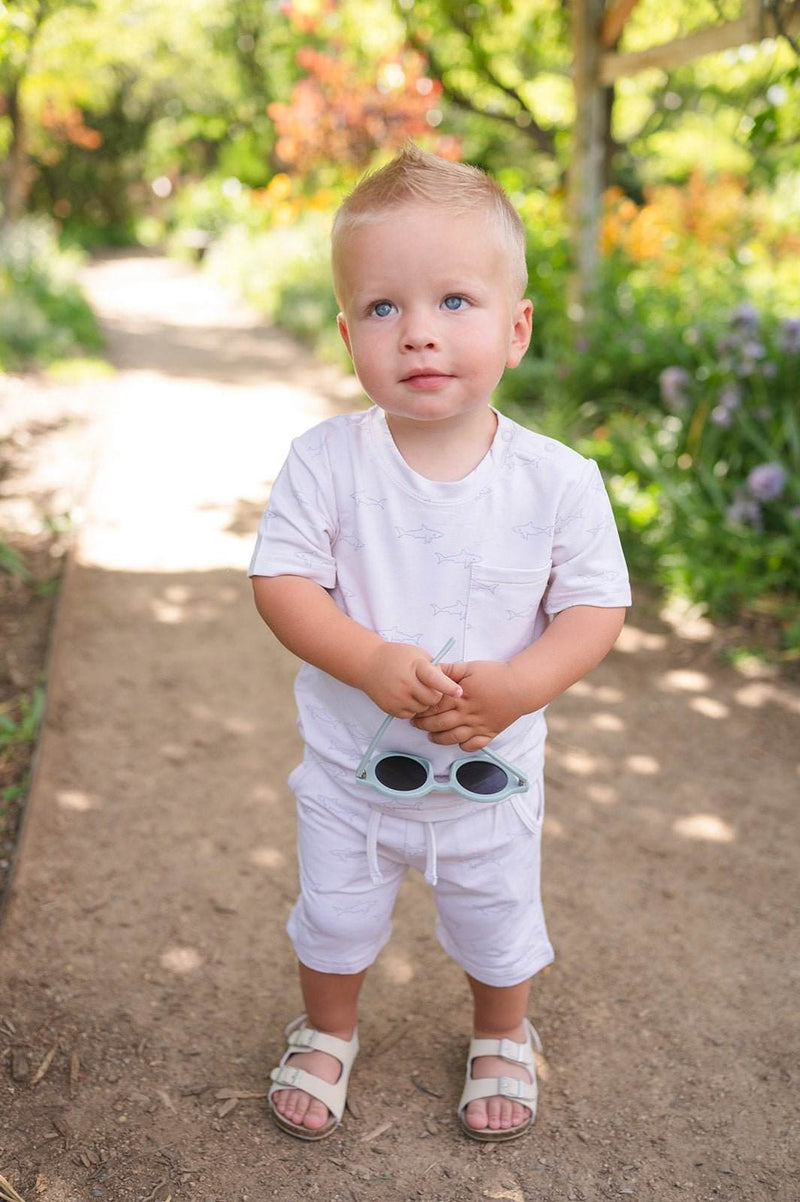 Toddler wearing a two-piece shark print short set in a garden path.