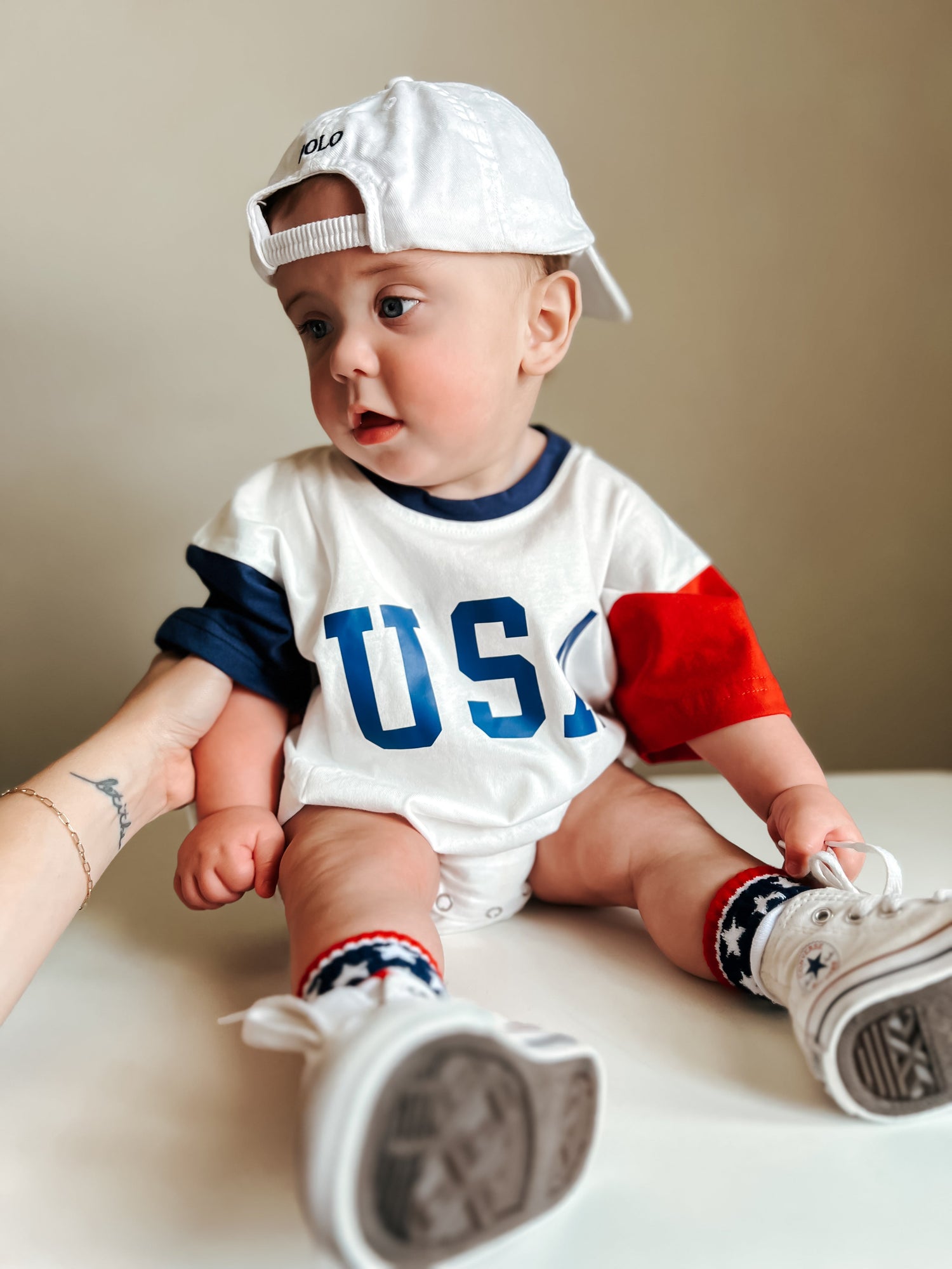 Baby wearing a red, white, and blue colorblock t-shirt romper from Little Joy Co., playing happily.