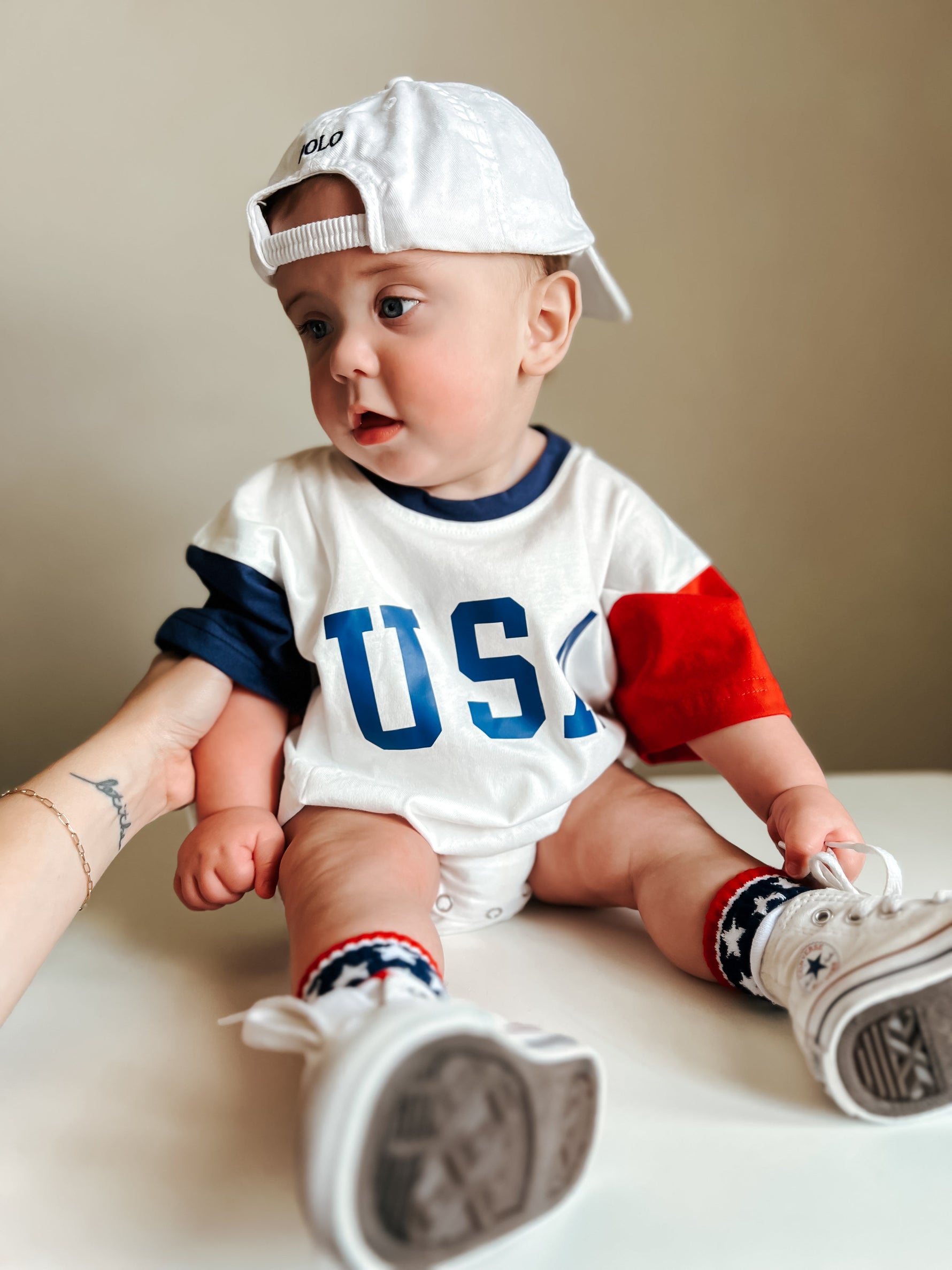 Baby wearing a red, white, and blue colorblock t-shirt romper from Little Joy Co., playing happily.