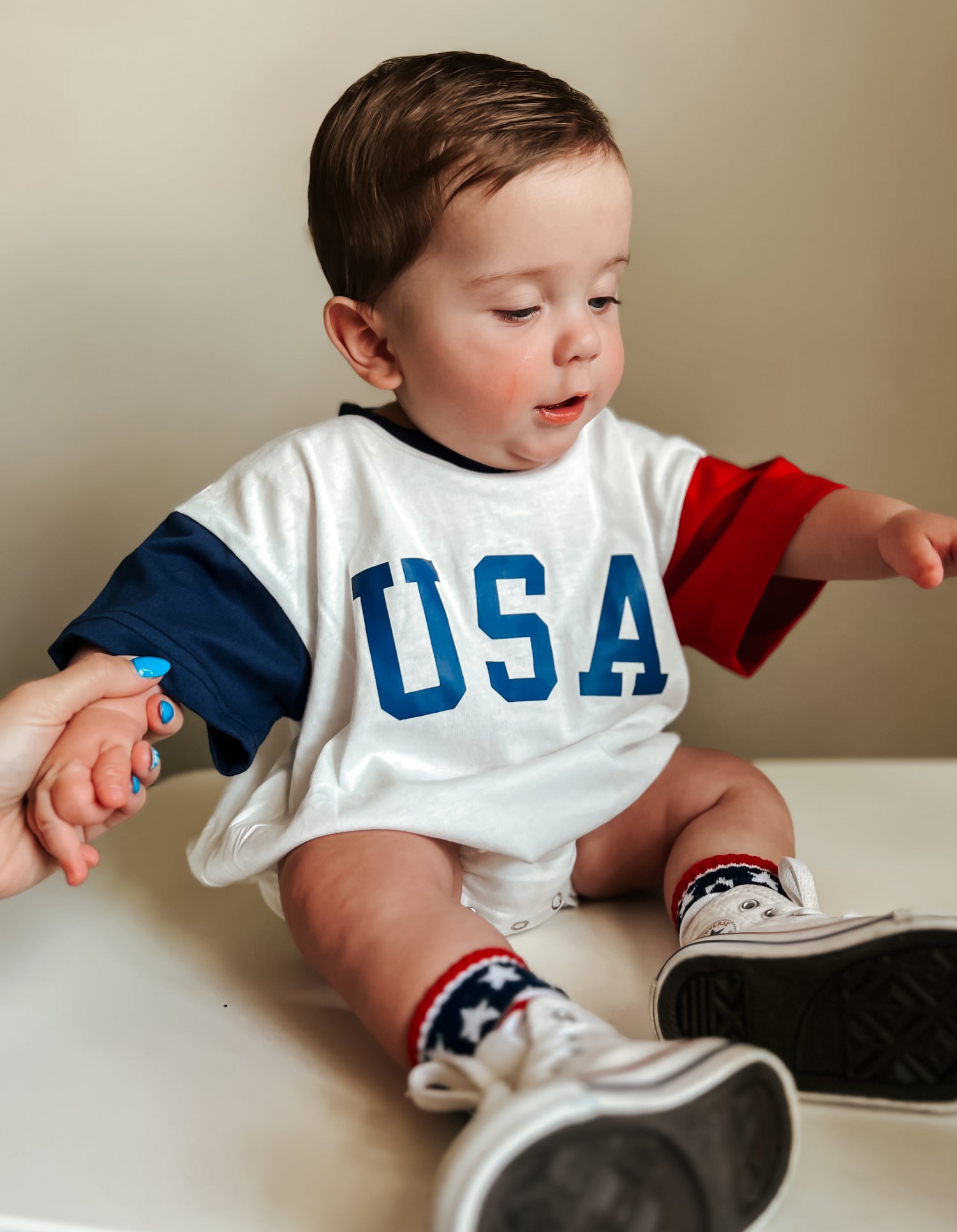 Baby wearing a red, white, and blue colorblock t-shirt romper from Little Joy Co., playing happily.