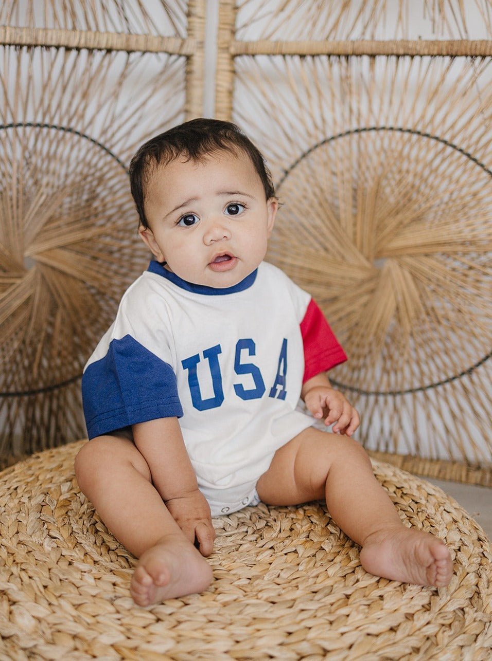 Baby wearing a red, white, and blue colorblock t-shirt romper from Little Joy Co., playing happily.