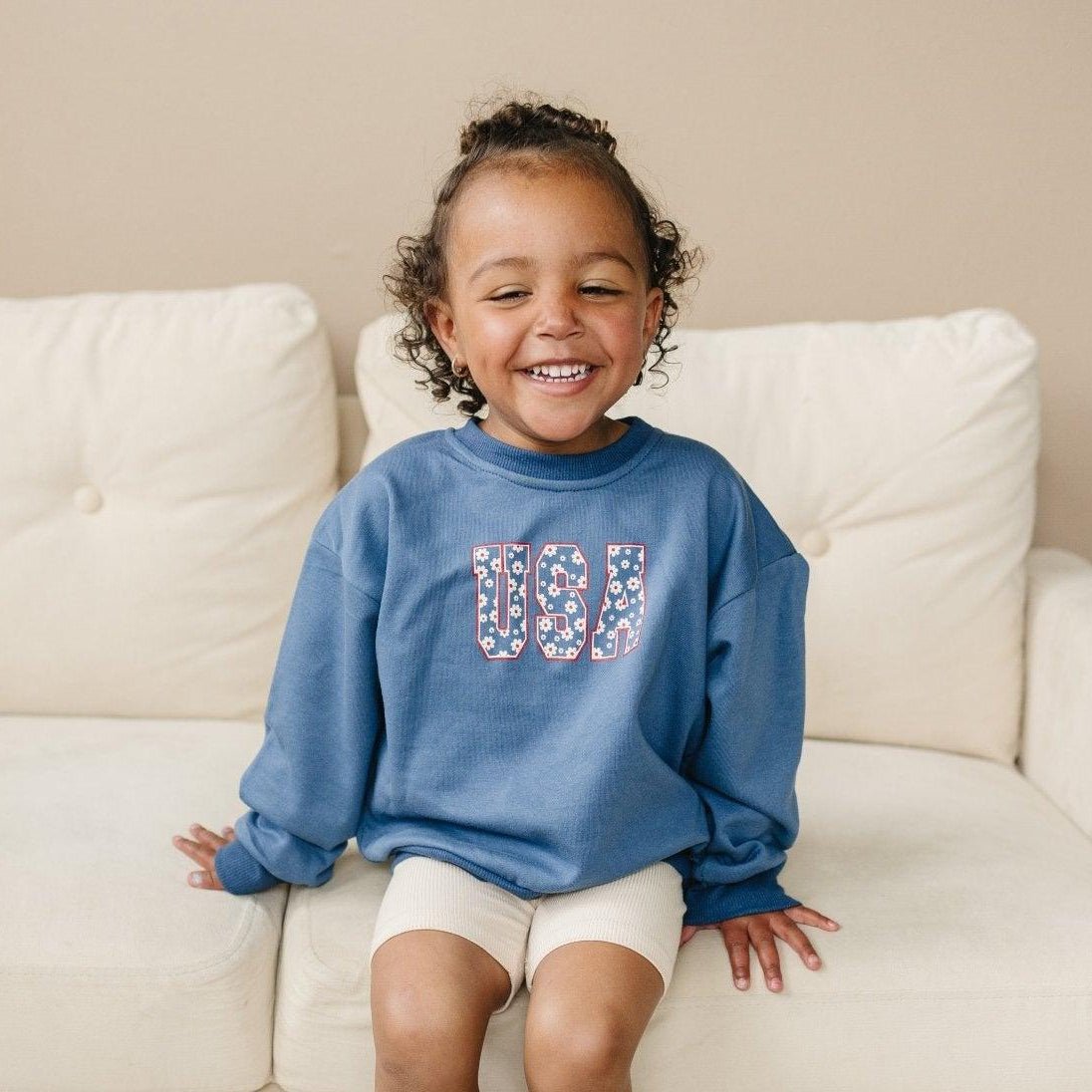 Close-up of a baby wearing a Little Joy Co. daisy graphic organic crewneck sweatshirt, smiling.