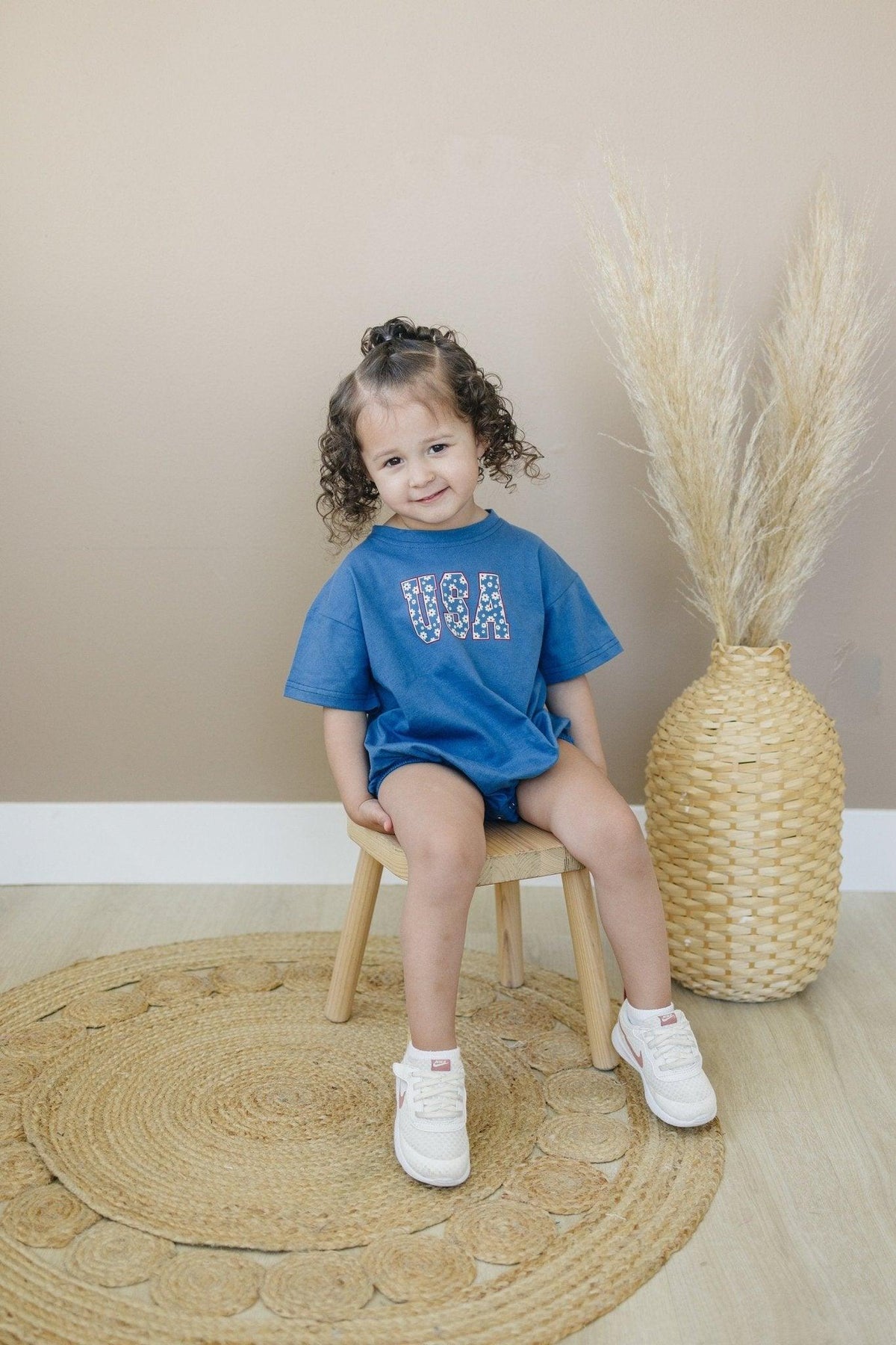 Little Joy Co. 100% cotton baby t-shirt romper in a neutral color, laid flat on a soft surface.
