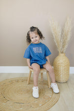 Little Joy Co. 100% cotton baby t-shirt romper in a neutral color, laid flat on a soft surface.