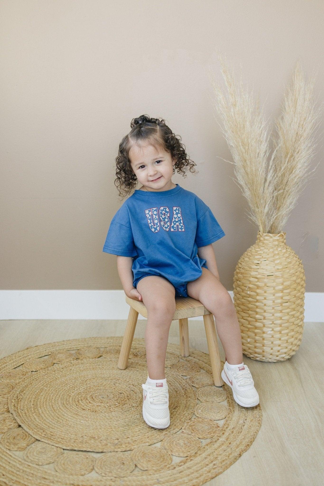 Little Joy Co. 100% cotton baby t-shirt romper in a neutral color, laid flat on a soft surface.