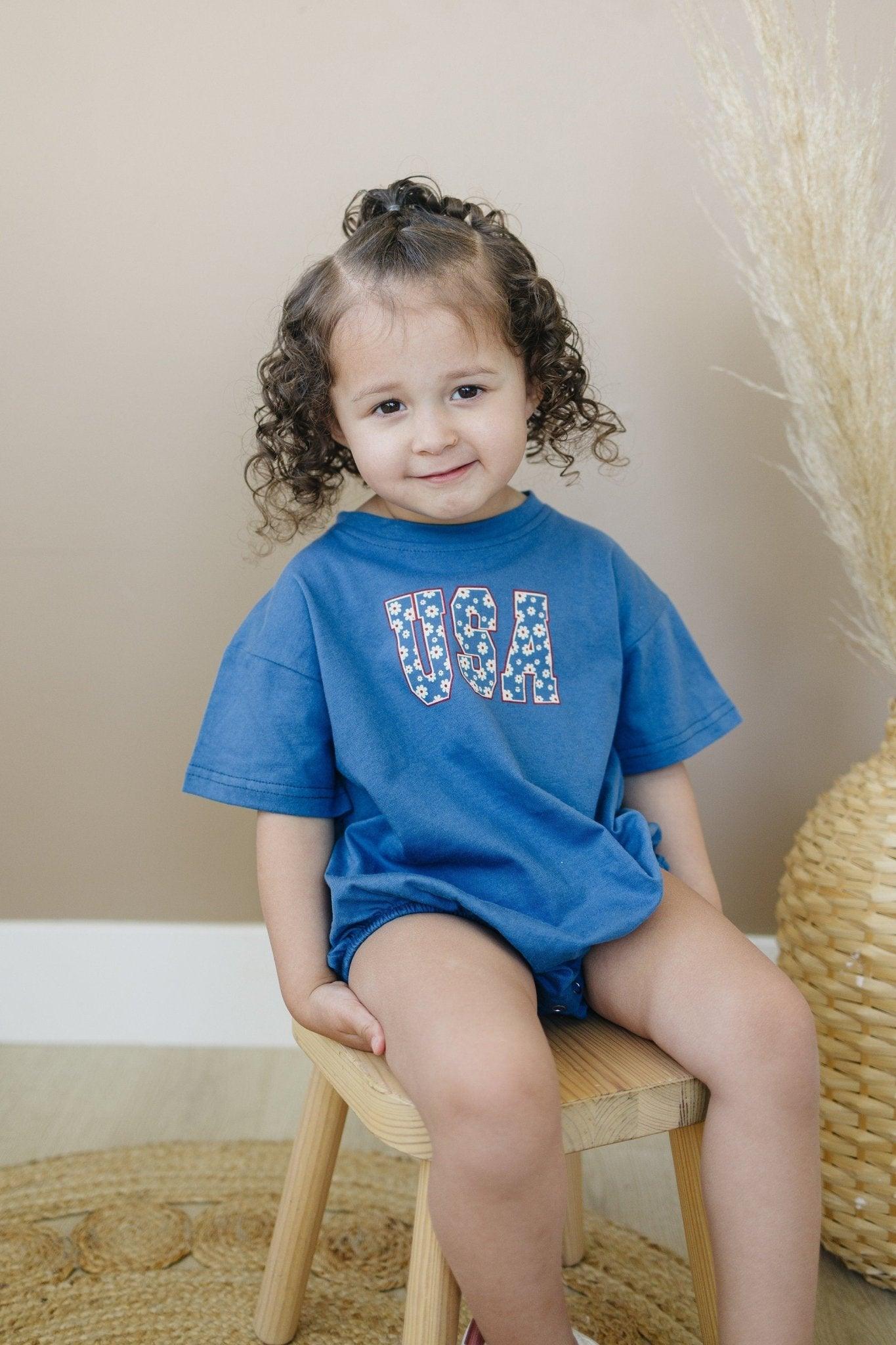 Little Joy Co. 100% cotton baby t-shirt romper in a neutral color, laid flat on a soft surface.
