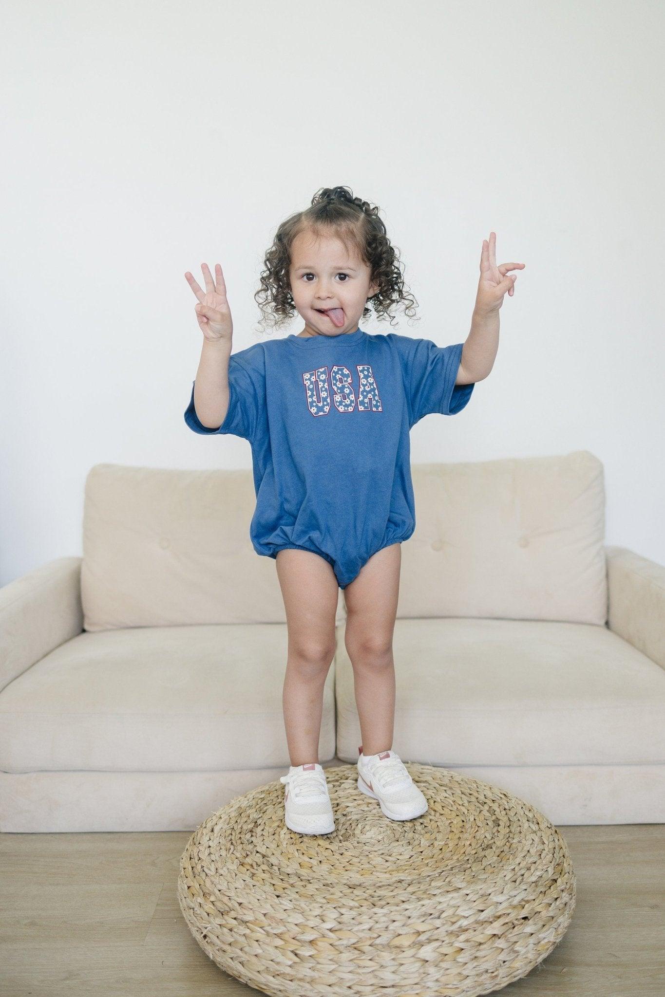 Little Joy Co. 100% cotton baby t-shirt romper in a neutral color, laid flat on a soft surface.