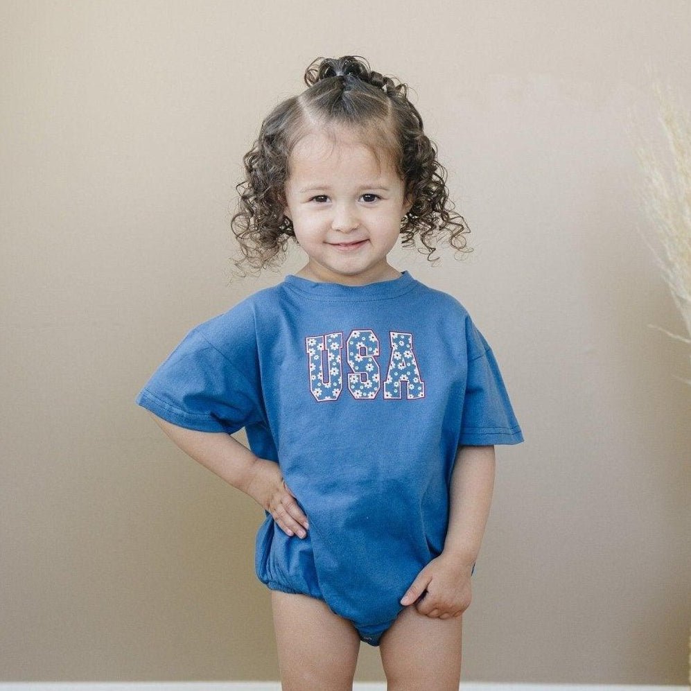 Little Joy Co. 100% cotton baby t-shirt romper in a neutral color, laid flat on a soft surface.