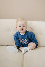 Little Joy Co. baby sweatshirt romper in ultra-soft organic terry fabric, light color, worn by a happy baby.