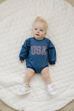Little Joy Co. baby sweatshirt romper in ultra-soft organic terry fabric, light color, worn by a happy baby.