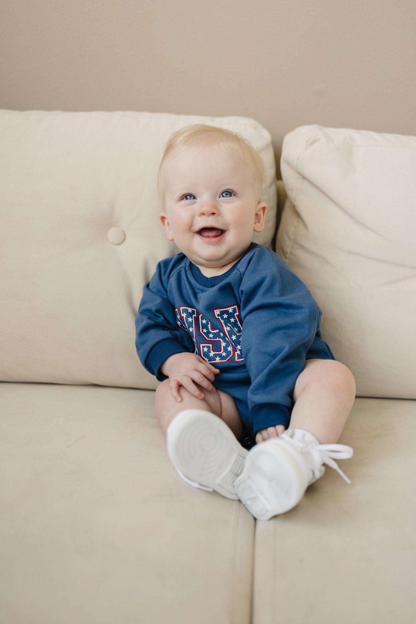Little Joy Co. baby sweatshirt romper in ultra-soft organic terry fabric, light color, worn by a happy baby.