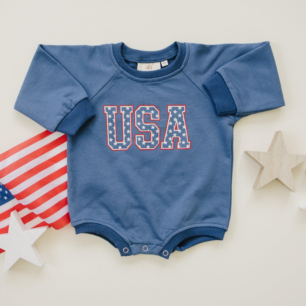 Little Joy Co. baby sweatshirt romper in ultra-soft organic terry fabric, light color, worn by a happy baby.