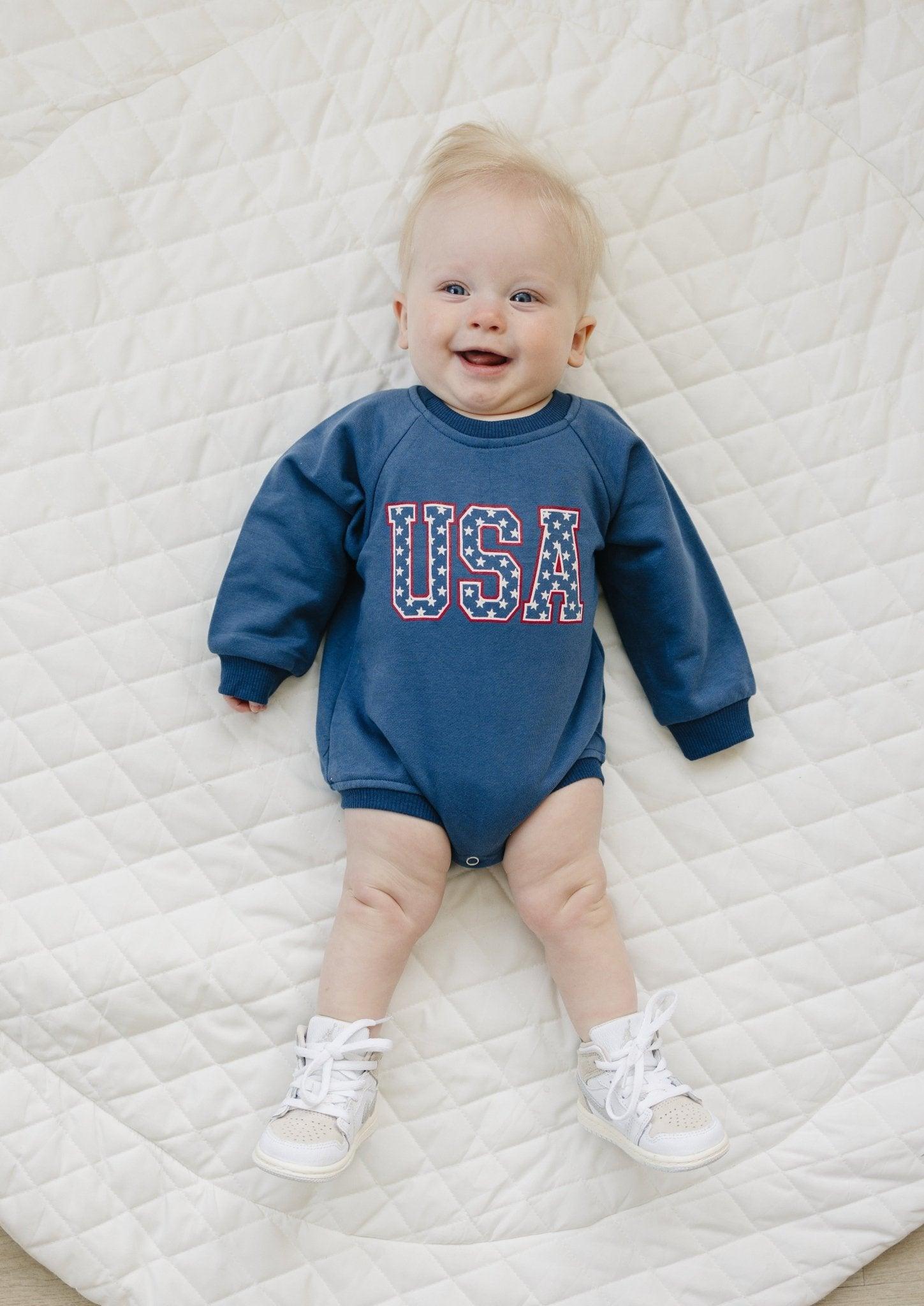 Little Joy Co. baby sweatshirt romper in ultra-soft organic terry fabric, light color, worn by a happy baby.